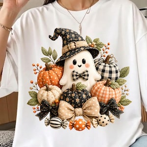 May include: A white t-shirt featuring a graphic of a smiling ghost wearing a black floral witch hat and a plaid bowtie, surrounded by various pumpkins in orange, white, and black patterns, green leaves, and decorative tan and black bows.