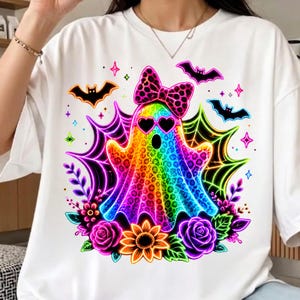 May include: A white t-shirt featuring a colourful, rainbow-hued ghost graphic with a leopard print pattern. The ghost wears heart-shaped sunglasses and a matching leopard print bow. It is surrounded by neon spiderwebs, bats, and flowers.