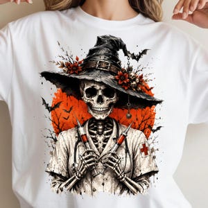 May include: A white t-shirt featuring a graphic of a skeleton dressed as a nurse, wearing a wide-brimmed black hat adorned with red flowers and skulls. The skeleton holds two syringes, with a red moon, bare tree branches, and bats in the background.