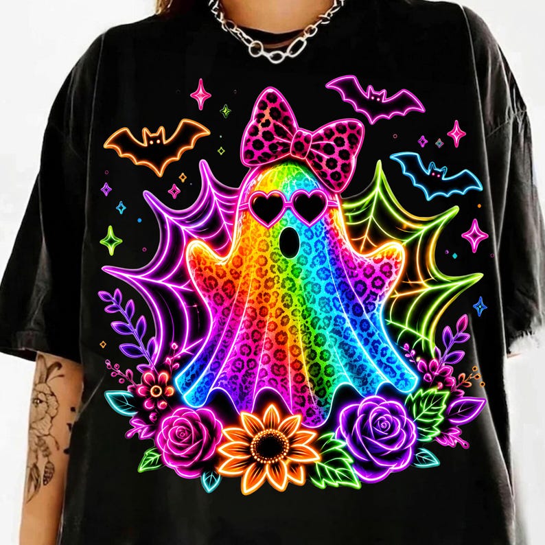 May include: A black t-shirt featuring a vibrant, rainbow-coloured ghost with a leopard print pattern. The ghost wears heart-shaped sunglasses and a matching leopard print bow. It is surrounded by neon spiderwebs, bats, roses, and a sunflower.