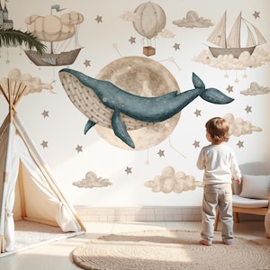 Könnte beinhalten: Ein Wandbild für das Kinderzimmer mit Illustrationen eines blauen Wals, eines Heißluftballons, eines Segelboots und eines Schlosses. Die Szene umfasst ein Tipi, ein Kind und einen runden Teppich. Die Farbpalette ist weich und gedämpft.