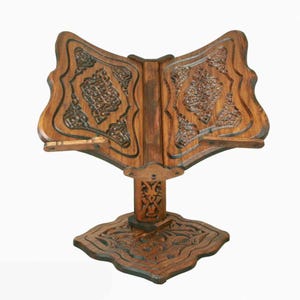 May include: A wooden book stand with intricate carvings. The stand is designed to hold a book open at an angle for easy reading. The stand is made of dark wood and has a traditional design.
