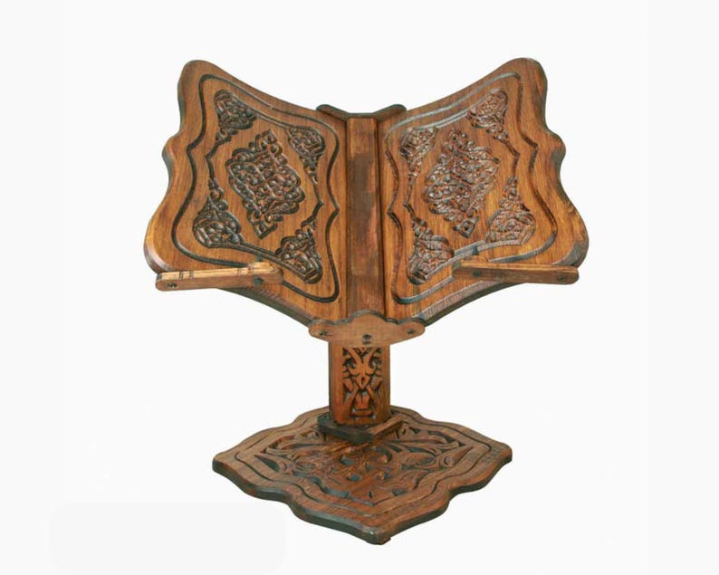 May include: A wooden book stand with intricate carvings. The stand is designed to hold a book open at an angle for easy reading. The stand is made of dark wood and has a traditional design.