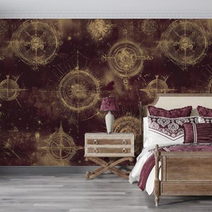 May include: A bedroom with a burgundy and gold compass-themed wallpaper. The room features a wooden bed frame with burgundy bedding, a nightstand with a lamp, and a light gray floor. The wallpaper has a distressed look.