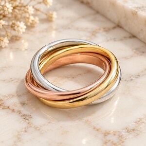 May include: A tri-color rolling ring featuring three interlocking bands in polished silver, yellow gold, and rose gold tones. The smooth, rounded metal bands are connected in a continuous loop, creating a layered effect with a reflective finish.