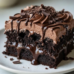 Puede incluir: Una rebanada de pastel de chocolate rico con glaseado de chocolate y virutas de chocolate. Salsa de chocolate negro gotea por los lados, creando un postre decadente. El pastel está en un plato blanco.