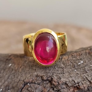 Pode incluir: Um anel de ouro com uma grande gema rosa oval e brilhante.