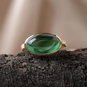 Pode incluir: Um anel de ouro com uma grande gema oval verde.