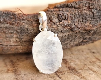 May include: A silver pendant featuring a clear, oval-shaped quartz crystal with a silver bail. The pendant is resting on a piece of weathered wood.