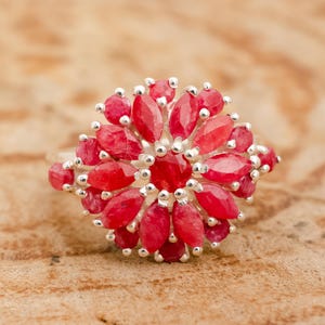 May include: A silver ring featuring a cluster of red ruby stones set in a flower design.