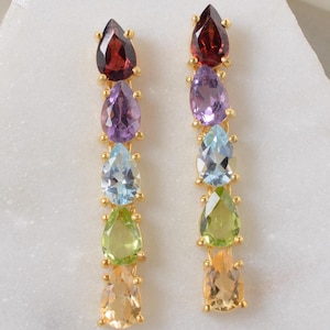 May include: A pair of gold earrings featuring a cascade of pear-shaped gemstones. The stones are arranged in a rainbow order, starting with garnet, amethyst, aquamarine, peridot, and citrine.