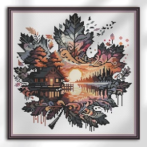 Puede incluir: Arte de punto de cruz de una escena de puesta de sol dentro de una forma de hoja de arce. La obra presenta una casa, árboles y un lago, todo en tonos de naranja, marrón y gris. La pieza está enmarcada en un marco marrón oscuro.
