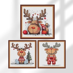 May include: Three framed cross-stitch artworks featuring cartoon reindeer. The reindeer have brown antlers, red noses, and are wearing festive outfits. One reindeer is sitting, another is lying down, and the third is standing.