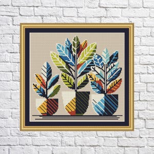 Puede incluir: Tres plantas en maceta estilizadas con hojas geométricas en tonos azules, verdes, amarillos y naranjas. Las macetas también son geométricas y presentan una variedad de colores.