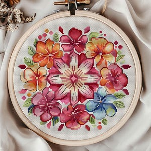 May include: A completed cross-stitch embroidery in a wooden hoop, showcasing a vibrant floral pattern. The flowers are in shades of red, pink, orange, and blue, with green foliage. The design is set against a white fabric background.