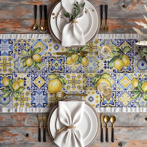 Peut inclure: Mise en place avec un chemin de table sur le thème des citrons. Le chemin de table présente un motif répété de citrons jaunes et de feuilles vertes sur un motif de carreaux bleus et blancs. Assiettes blanches, serviettes et couverts dorés.