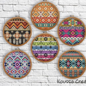 May include: Six round embroidery hoops with colorful geometric patterns in various designs. The patterns feature a mix of vibrant colors including orange, teal, pink, and purple. The hoops are displayed against a white brick wall. The text "Noussa Creation" is at the bottom.
