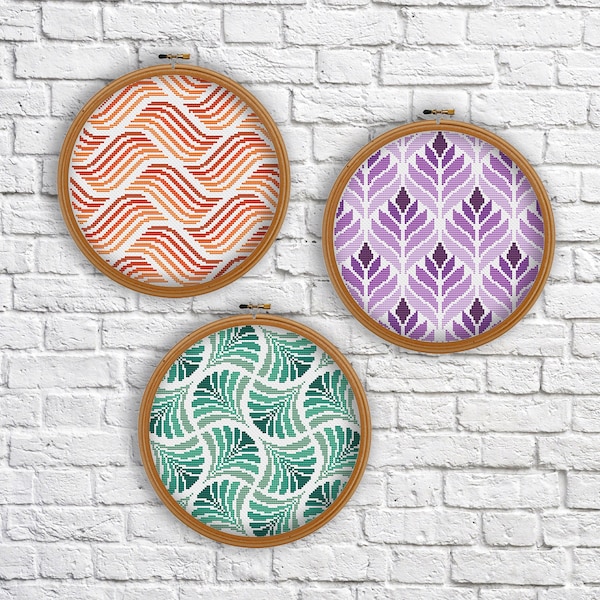 May include: Three embroidery hoops with different geometric patterns. The hoops are made of wood and have a natural finish. The patterns are a red and orange wave pattern, a purple floral pattern, and a green leaf pattern.