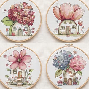 Pode incluir: Quatro bastidores de bordado circulares de madeira com padrões de ponto cruz de pequenas casas coroadas por grandes flores coloridas. Os desenhos apresentam motivos florais em rosa, azul e vermelho, folhas verdes e detalhes sobre tecido branco.