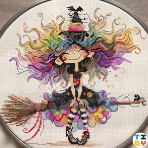 Puede incluir: Un diseño de punto de cruz de una bruja caprichosa con cabello colorido y un sombrero negro, montada en una escoba. La bruja está sonriendo, y el diseño presenta morados, amarillos y verdes vibrantes. La obra de arte está enmarcada en un aro de metal.