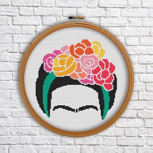 May include: A cross-stitch embroidery hoop with a colorful floral design on a black background. The design is a portrait of Frida Kahlo with a flower crown.