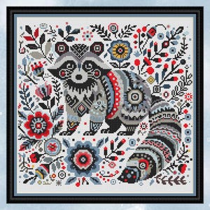 May include: Cross-stitch design showing a raccoon surrounded by flowers and foliage. The raccoon is in grey, black, and white, with red and blue details. The flowers and leaves are red, blue, and green, set against a white background, framed in black.