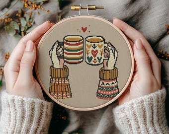 May include: Cross stitch pattern of two hands holding mugs of coffee or tea. The mugs are decorated with a festive, wintery design. The hands are wearing cozy, patterned mittens.