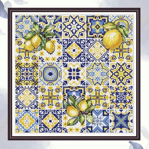 Op de afbeelding: Een ingelijst kruissteekkunstwerk met een patchworkontwerp van blauwe, gele en witte tegels. De tegels hebben geometrische patronen en citroentakken. Het kunstwerk zit in een donkerbruine lijst.