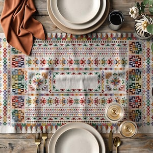 Può includere: Un runner da tavolo colorato con sfondo bianco e disegni geometrici e floreali in rosso, verde, giallo e blu. Il runner è posizionato su un tavolo di legno con piatti, posate e bicchieri.