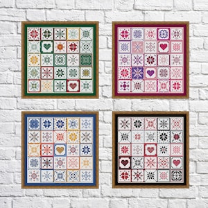 Op de afbeelding: Vier ingelijste kruissteek-samplers tegen een witte bakstenen muur. Elke sampler toont een raster van kleurrijke, geometrische patronen, waaronder harten, sneeuwvlokken en bloemmotieven. De lijsten zijn groen, bordeaux, blauw en zwart.