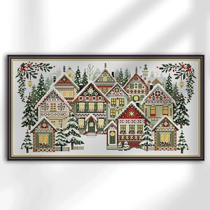 May include: Framed cross-stitch depicting a winter village. The artwork shows several colourful houses with snow-covered roofs and evergreen trees. The houses have red, green, and yellow accents, framed with green foliage.