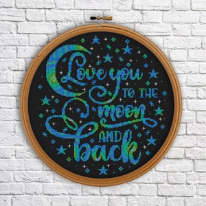 Puede incluir: Un aro de bordado negro con un diseño de luna y estrellas azul y verde. El texto "Love you to the moon and back" está bordado en una fuente cursiva.