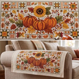 May include: A rectangular fabric runner featuring a cross-stitch design of three orange pumpkins, a large yellow sunflower, and various autumn leaves, acorns, and berries. The border consists of geometric star patterns in green and orange.