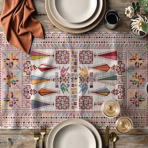 Peut inclure: Un chemin de table blanc avec un motif géométrique coloré en rouge, bleu, vert, jaune et orange. Le chemin de table est posé sur une table en bois avec deux assiettes blanches, deux verres à bord doré et deux fourchettes dorées.