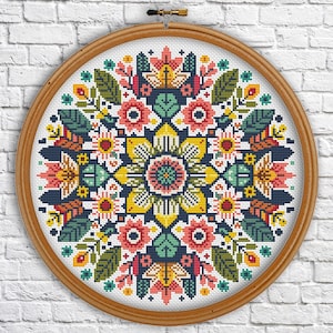May include: A colorful floral mandala cross stitch pattern in a round wooden embroidery hoop. The design features a variety of flowers, leaves, and geometric shapes in shades of pink, yellow, green, and blue.