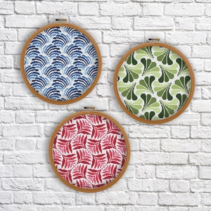 May include: Three embroidery hoops featuring different geometric patterns. The hoop on the left has a blue and white design, the middle hoop has a green and white design, and the hoop on the right has a red and white design.
