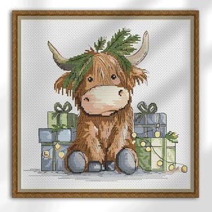 May include: Cross-stitch image of a Highland cow wearing a fir branch crown, sitting in front of wrapped gifts. The gifts are in shades of blue and green, with string lights. The artwork is framed in a wooden frame.