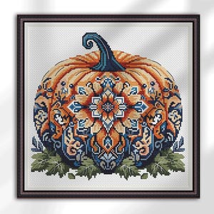 Puede incluir: Arte de punto de cruz de una calabaza con un intrincado diseño de mandala. La calabaza es naranja con un tallo azul oscuro y está rodeada de hojas verdes. El mandala presenta patrones naranjas y azules.