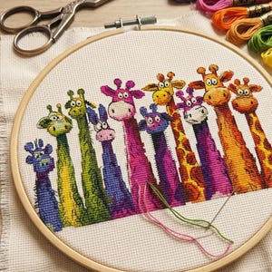 Op de afbeelding: Een kleurrijke kruissteek borduurring met een rij cartoon giraffen. De giraffen hebben lange halzen en lachen. De borduurring is van hout en bevat een schaar en draden.