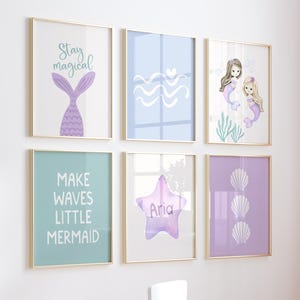 May include: A set of six framed mermaid-themed art prints in pastel colors. The prints feature mermaid tails, waves, shells, and mermaids. Text includes "Stay magical" and "Make waves little mermaid". The art is displayed on a white wall.