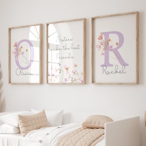 May include: Three framed prints with floral designs and the text "Sisters make the best friends" in the centre print. The left print features the letter "O" with the name "Olivia" below. The right print features the letter "R" with the name "Rachel" below.