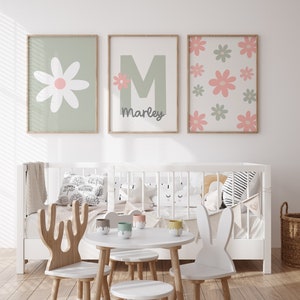 May include: Three framed prints with a green background and pink flowers. The center print has a large green letter M with a small pink flower and the name Marley below it. The print on the left has a large white flower with a pink center. The print on the right has a pattern of pink and green flowers.
