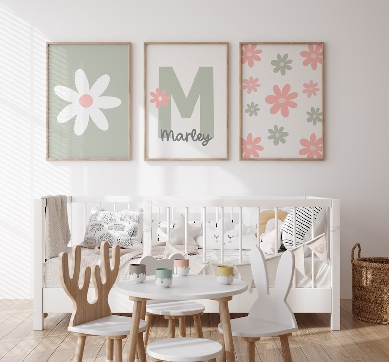May include: Three framed prints with a green background and pink flowers. The center print has a large green letter M with a small pink flower and the name Marley below it. The print on the left has a large white flower with a pink center. The print on the right has a pattern of pink and green flowers.