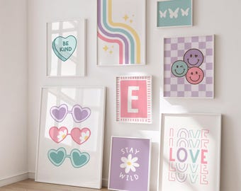 May include: A collection of framed art prints with various designs. Prints include a heart-shaped candy with "BE KIND", heart-shaped sunglasses, a rainbow design, butterflies, smiley faces, the letter "E", a daisy with "STAY WILD", and the word "LOVE".