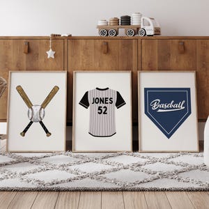 May include: Three framed baseball-themed prints. One features a baseball and crossed bats, another a jersey with "JONES 52", and the last a blue home plate with "Baseball" text. The prints are displayed on a wooden cabinet.