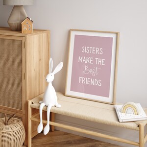 May include: A white rabbit figurine with long legs sits on a light wood bench. A framed print with the text "Sisters make the best friends" hangs on a light pink wall.