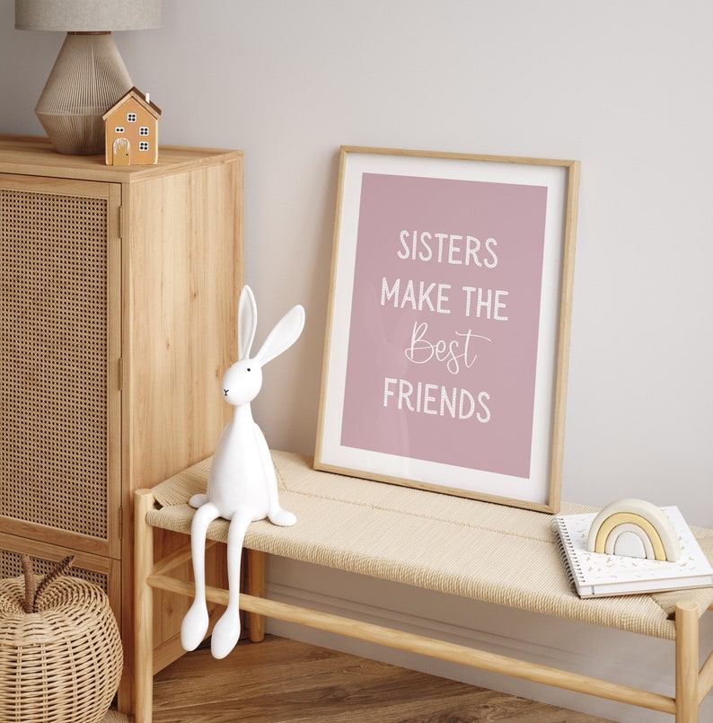 May include: A white rabbit figurine with long legs sits on a light wood bench. A framed print with the text "Sisters make the best friends" hangs on a light pink wall.