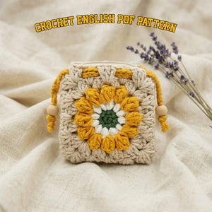 May include: A crocheted square pouch with a sunflower design. The sunflower has yellow petals, a white center, and a green core. The pouch is beige with yellow drawstrings and wooden beads. Text at the top reads "CROCHET ENGLISH PDF PATTERN".