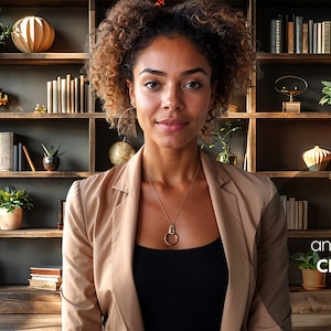 Puede incluir: Una mujer con el pelo rizado casta&ntilde;o lleva una chaqueta beige sobre una camiseta negra. Est&aacute; de pie frente a una estanter&iacute;a llena de libros, plantas y objetos decorativos. El texto "and LIGHT Clothing." es visible en la esquina inferior derecha de la imagen.