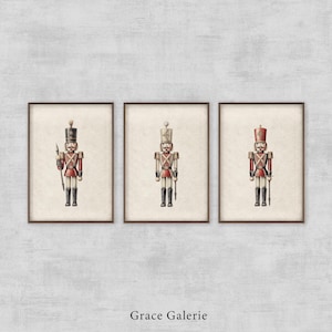 Puede incluir: Tres impresiones enmarcadas de soldados de juguete vintage. Cada impresión presenta un soldado diferente con un uniforme rojo y negro sosteniendo un rifle. Las impresiones están todas en un marco blanco con un passe-partout marrón.